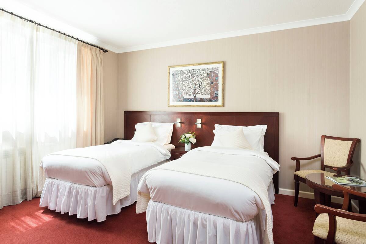 Ein Hotelzimmer mit zwei Betten, einem Holzkopfteil, einem kleinen Tisch und einem gerahmten Bild an der Wand.