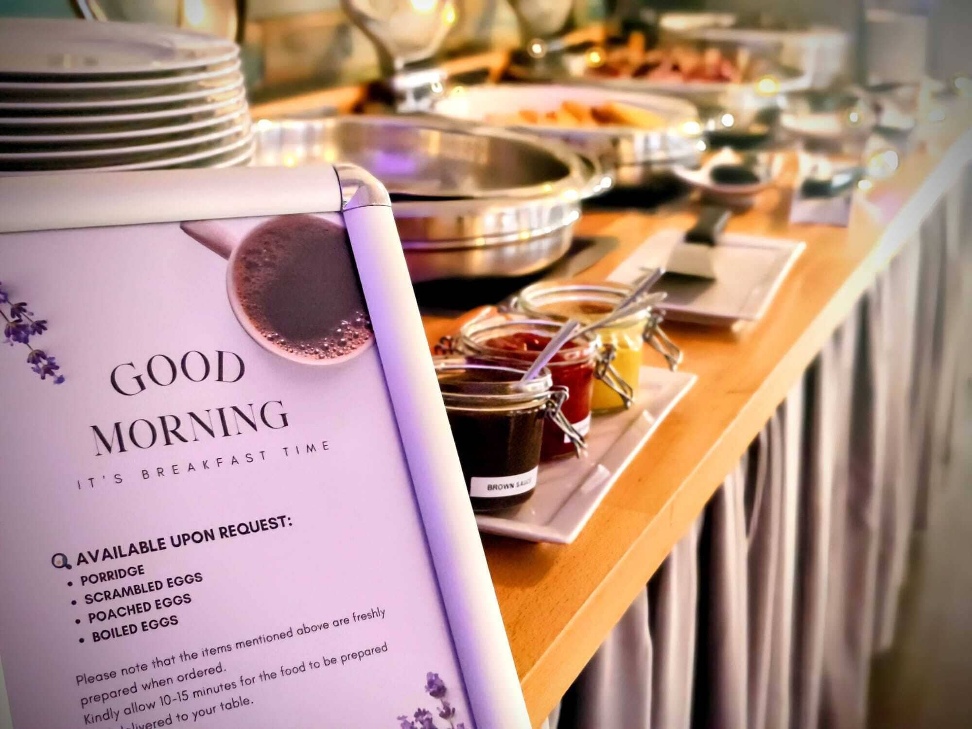 Un bufé de desayuno con un cartel que enumera los alimentos disponibles, como gachas, huevos revueltos, huevos pochados y huevos cocidos.