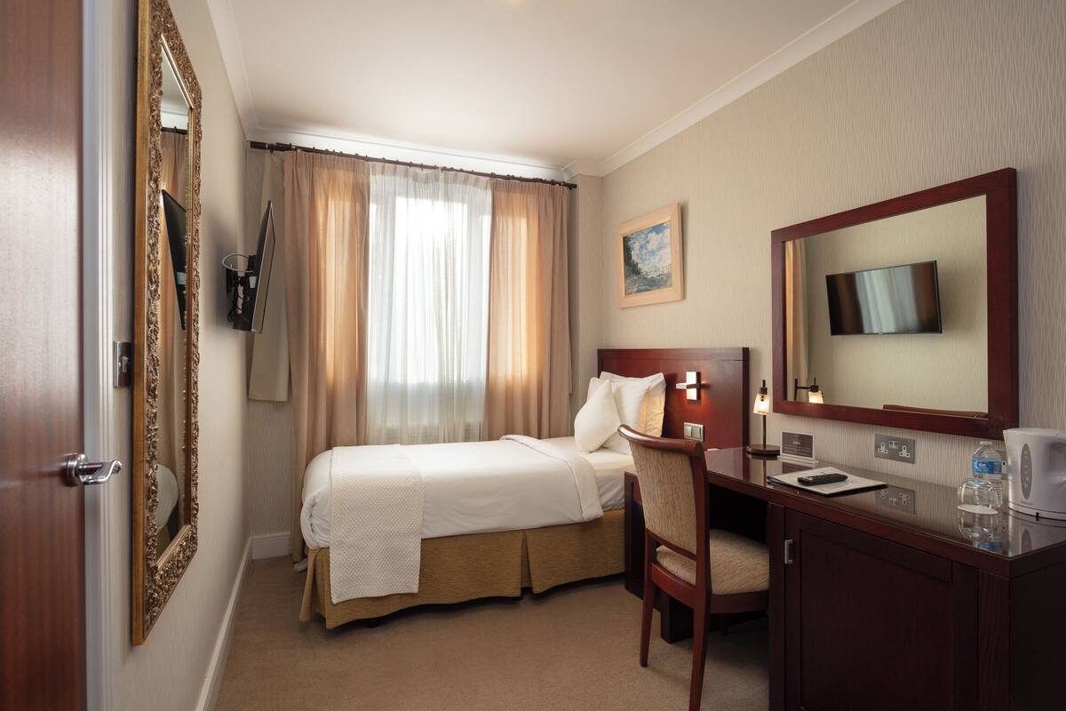 Ein Hotelzimmer mit Bett, Schreibtisch, Stuhl, Fernseher und einem Gemälde an der Wand.