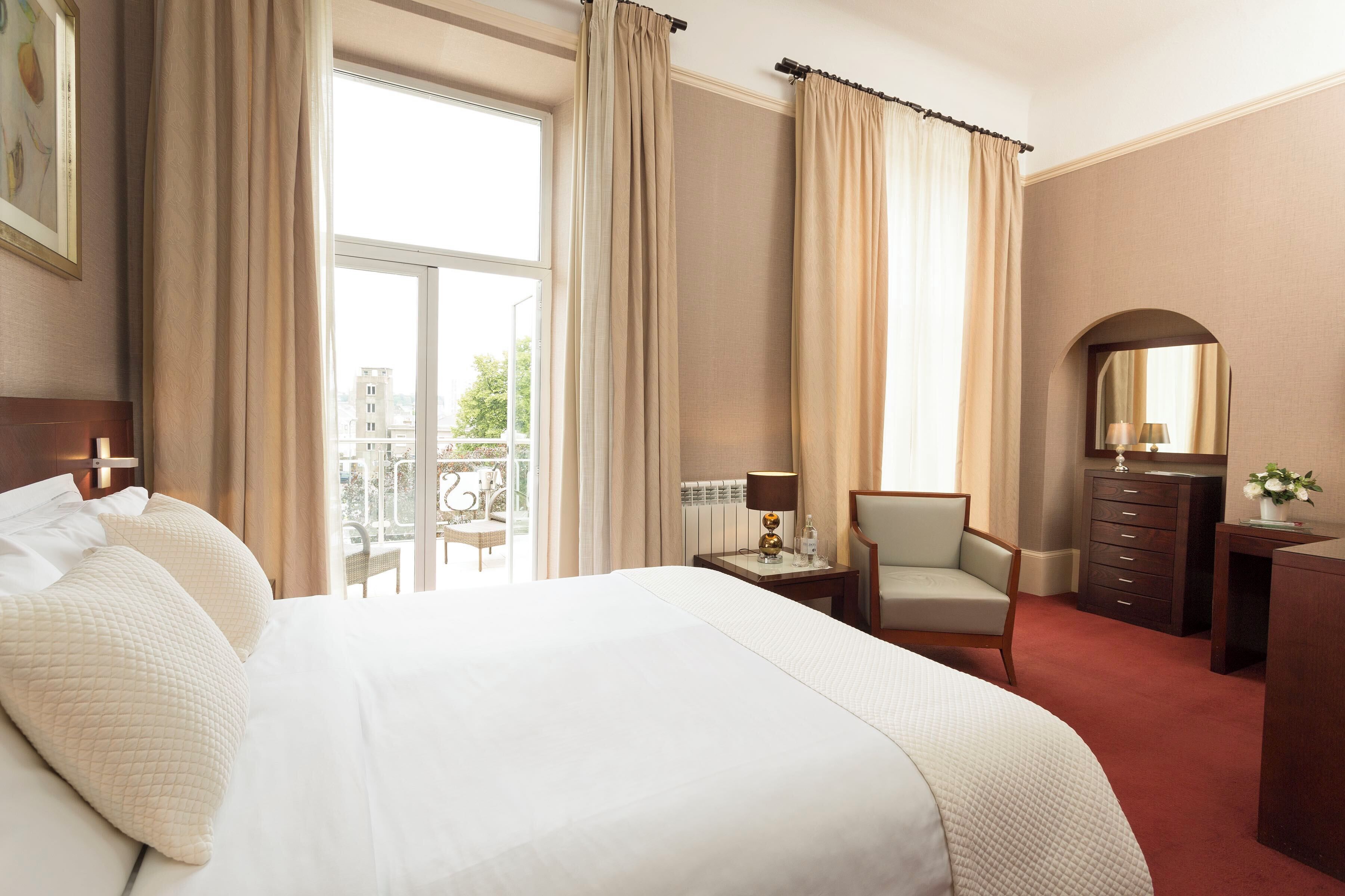 Habitaci ón de hotel con una cama grande, una silla, un escritorio, un aparador y una ventana con cortinas.