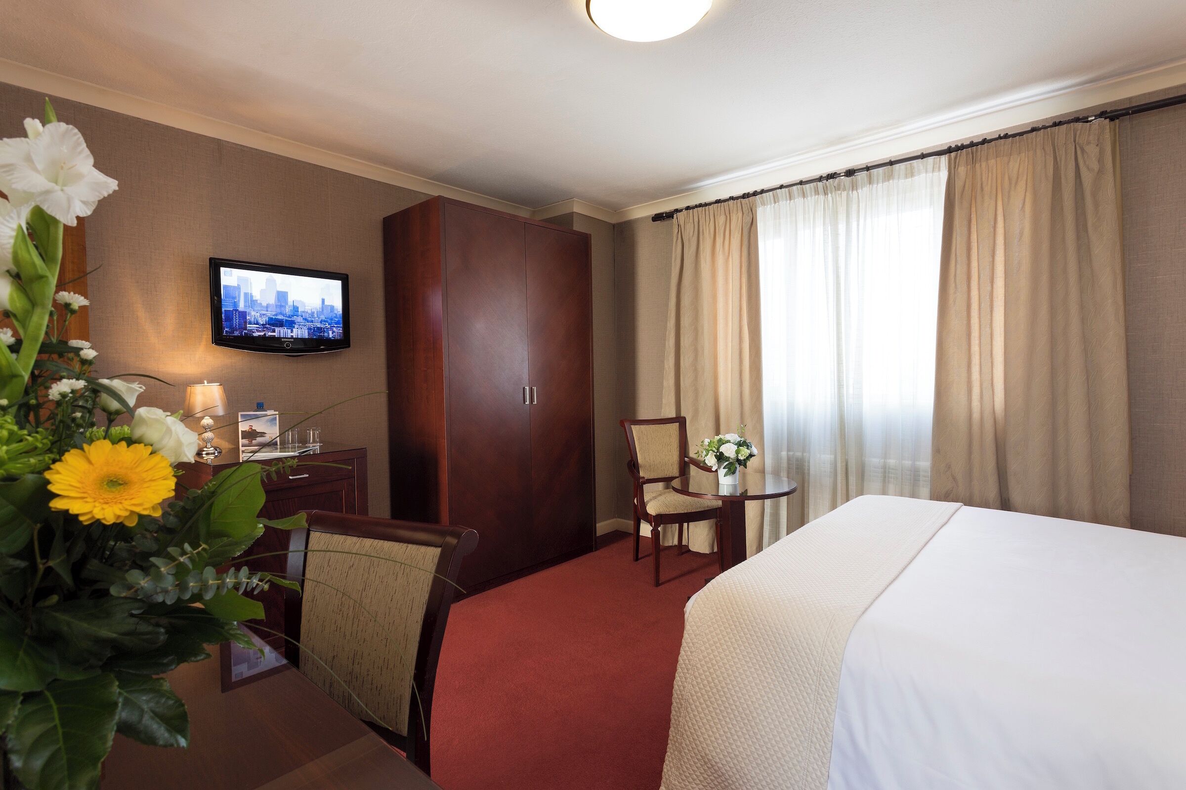 A hotel room with a bed, a desk with a chair, a television, and a window with curtains.