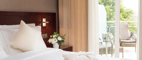 A hotel room with a bed, pillows, a nightstand with a vase of flowers, and a view of the outdoor balcony.