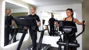A gym with treadmills and elliptical machines, a mirror reflecting the room, and a white brick wall.