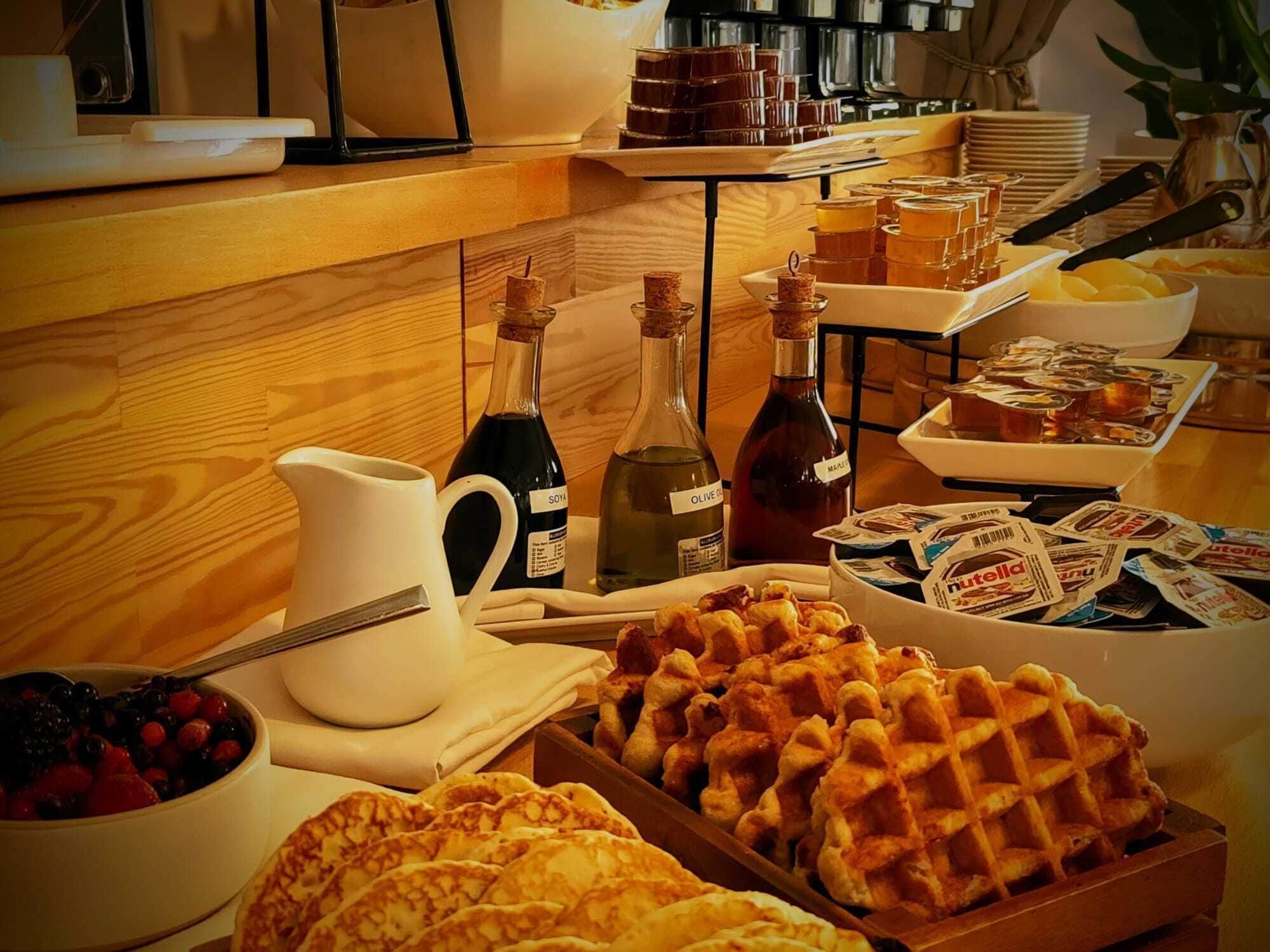 A breakfast buffet with waffles, pastries, and various condiments.