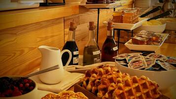A breakfast buffet with waffles, pastries, and various condiments.