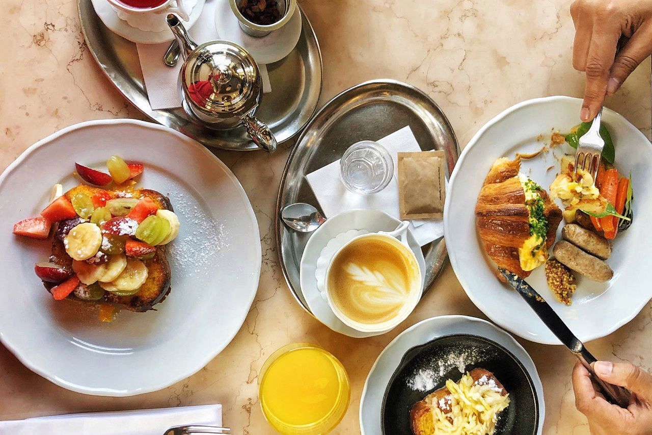 A breakfast setting with plates of food, a cup of coffee, and a teapot on a table.
