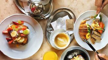 A breakfast setting with plates of food, a cup of coffee, and a teapot on a table.
