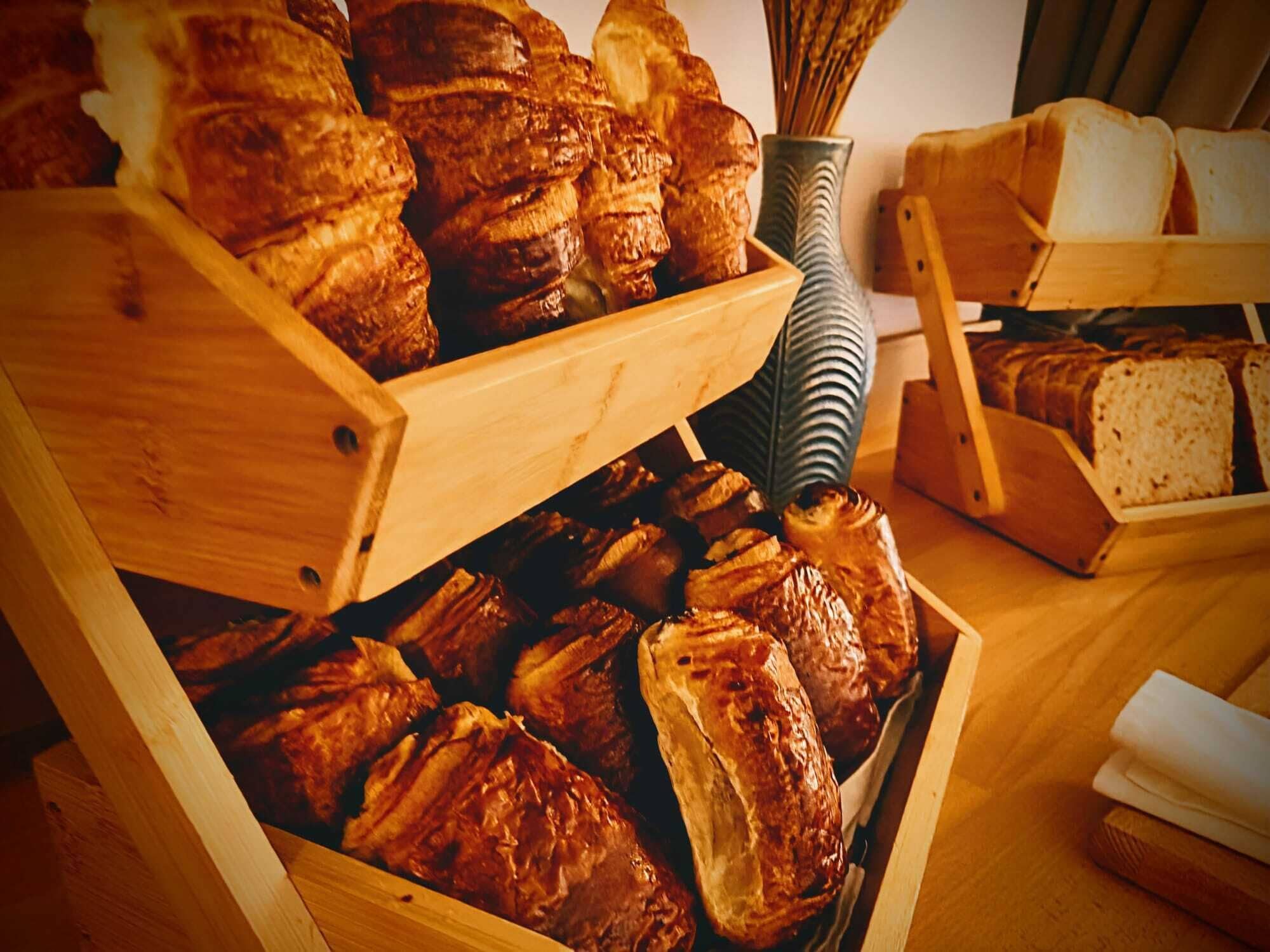 A wooden bread display with various types of bread, including baguettes and rolls, in a bakery setting.