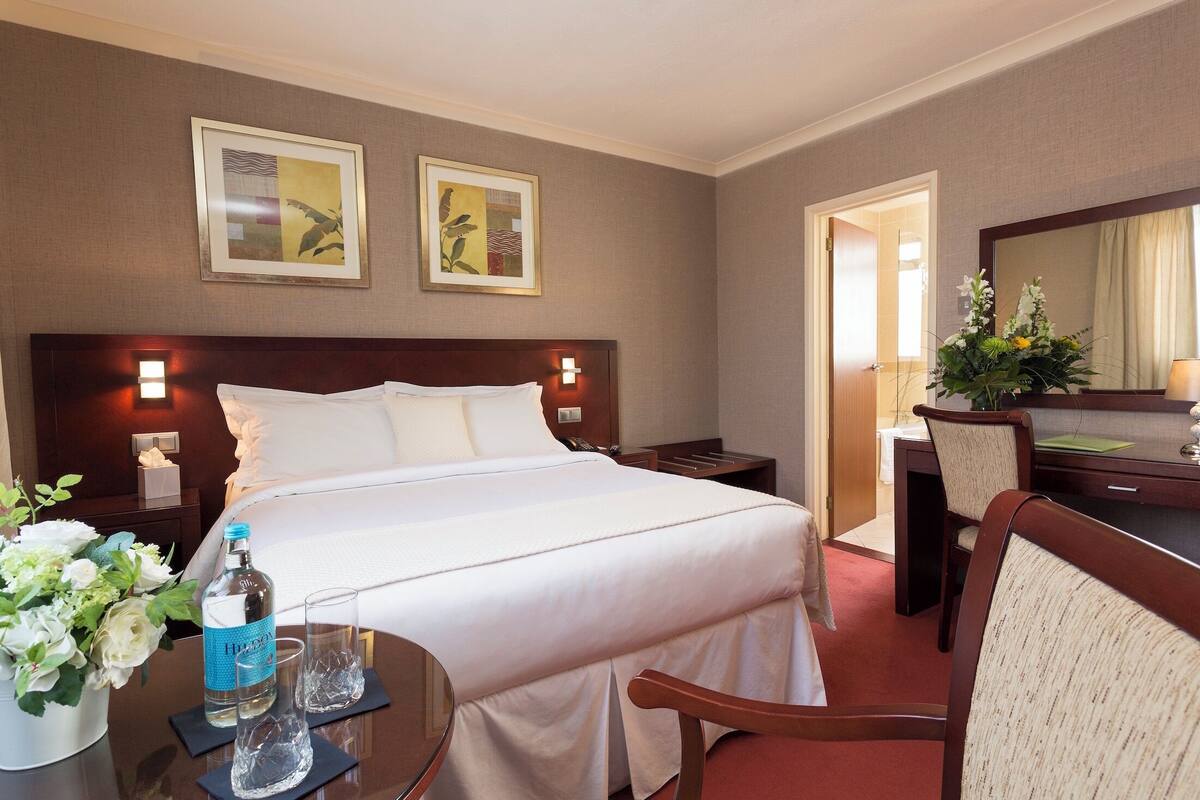 Ein Hotelzimmer mit einem großen Bett, einem Schreibtisch mit Stuhl, einem Spiegel und zwei gerahmten Bildern an der Wand.