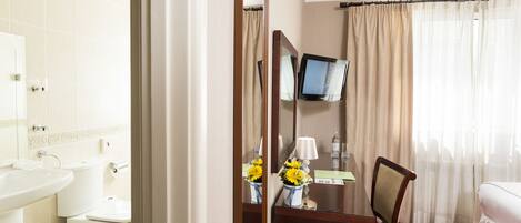 A hotel room with a bed, a desk with a chair, a TV, a bathroom with a sink and toilet, and a mirror.