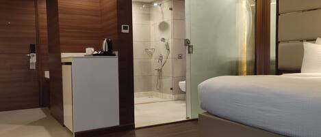 A hotel room with a bed, a small desk with a coffee maker, a shower area, and a toilet.