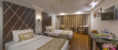 A hotel room with two beds, a desk with a computer, a chair, and a dining table with food and drinks.