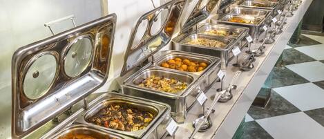 Una barra de buffet con varias estaciones de comida, cada una con un recipiente metálico y una cuchara.
