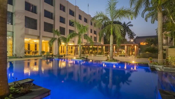 Een hotel met een zwembad, palmbomen en een goed verlichte gevel.