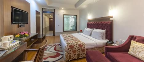 A hotel room with a bed, a desk with a TV, a red sofa, and a dining table with fruit.