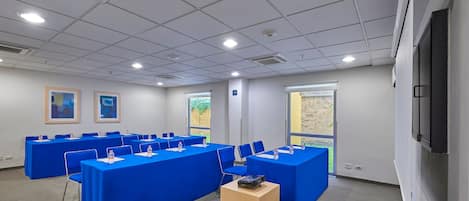 Un salón de conferencias con varias mesas, sillas y una pantalla para proyector.