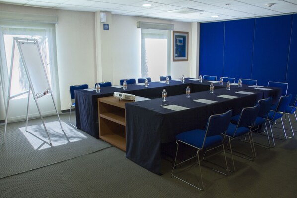 Une salle de conférence avec une longue table, des chaises bleues et des bouteilles d’eau.