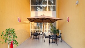 An outdoor patio with tables and chairs, a large umbrella, and a potted plant. - City Express by Marriott Tepotzotlan (Tepotzotlán)