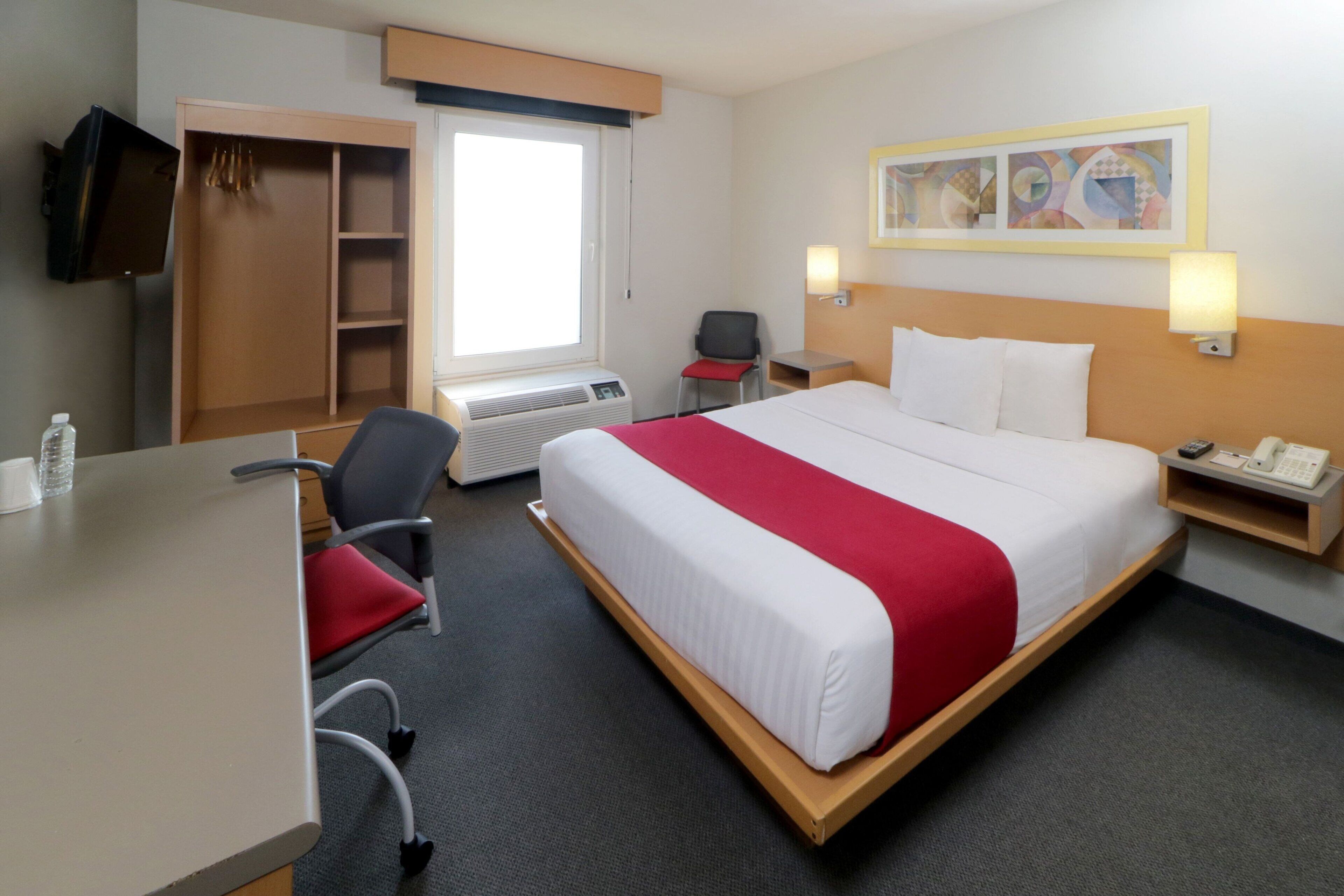 A hotel room with a bed, a desk, a chair, a wardrobe, a television, and a window.