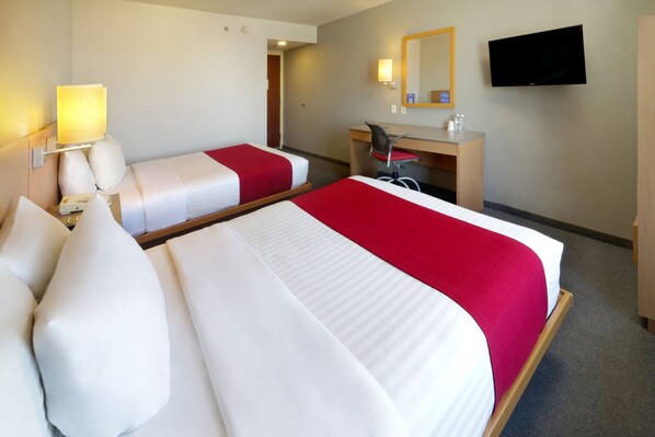 Une chambre d’hôtel avec deux lits, un bureau, une chaise, une télévision et un miroir.