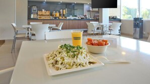 A dining area with a table, chairs, a meal, a drink, and a counter with a TV in the background. - City Express by Marriott Tepotzotlan (Tepotzotlán)