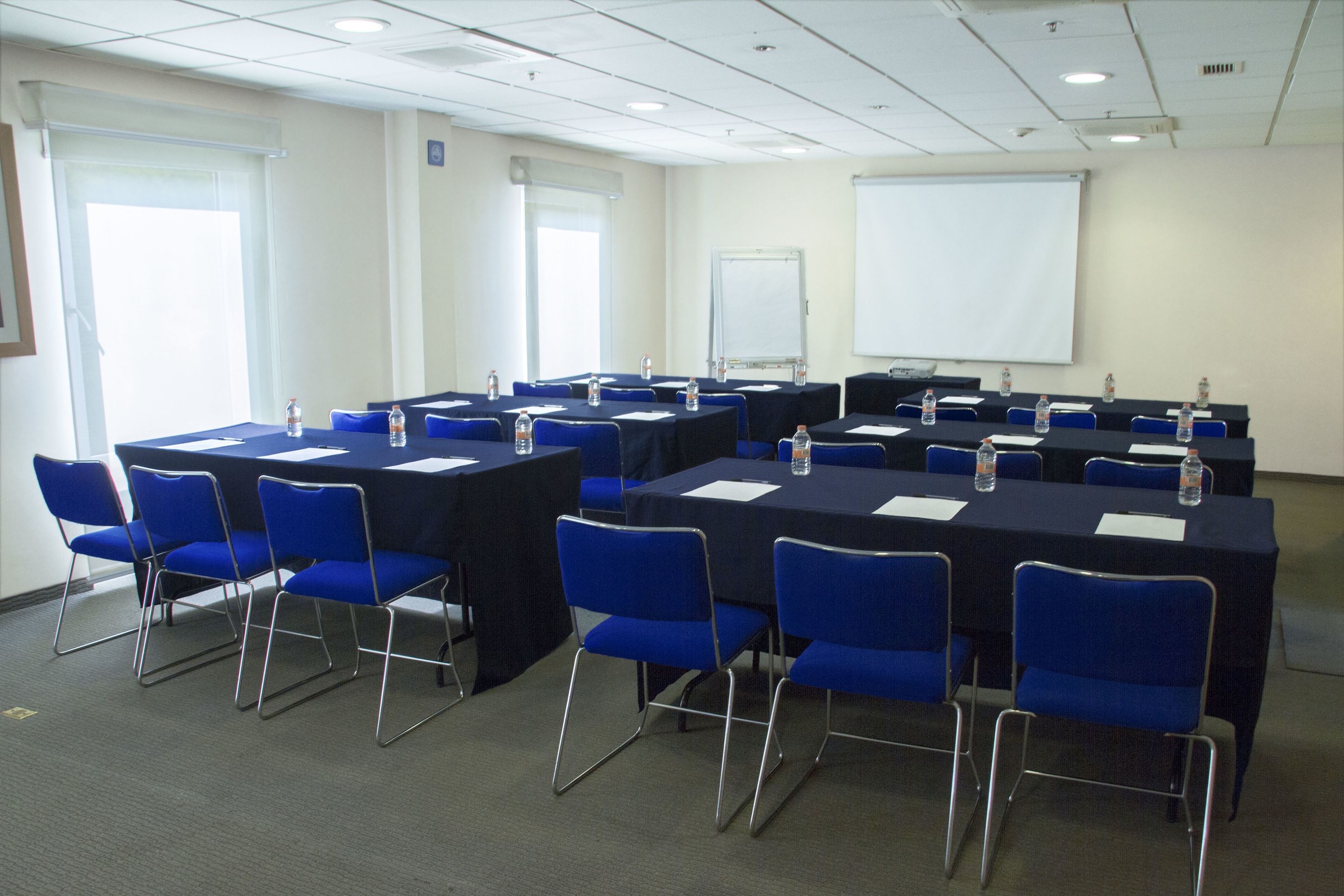 A conference room with multiple tables, blue chairs, and water bottles.