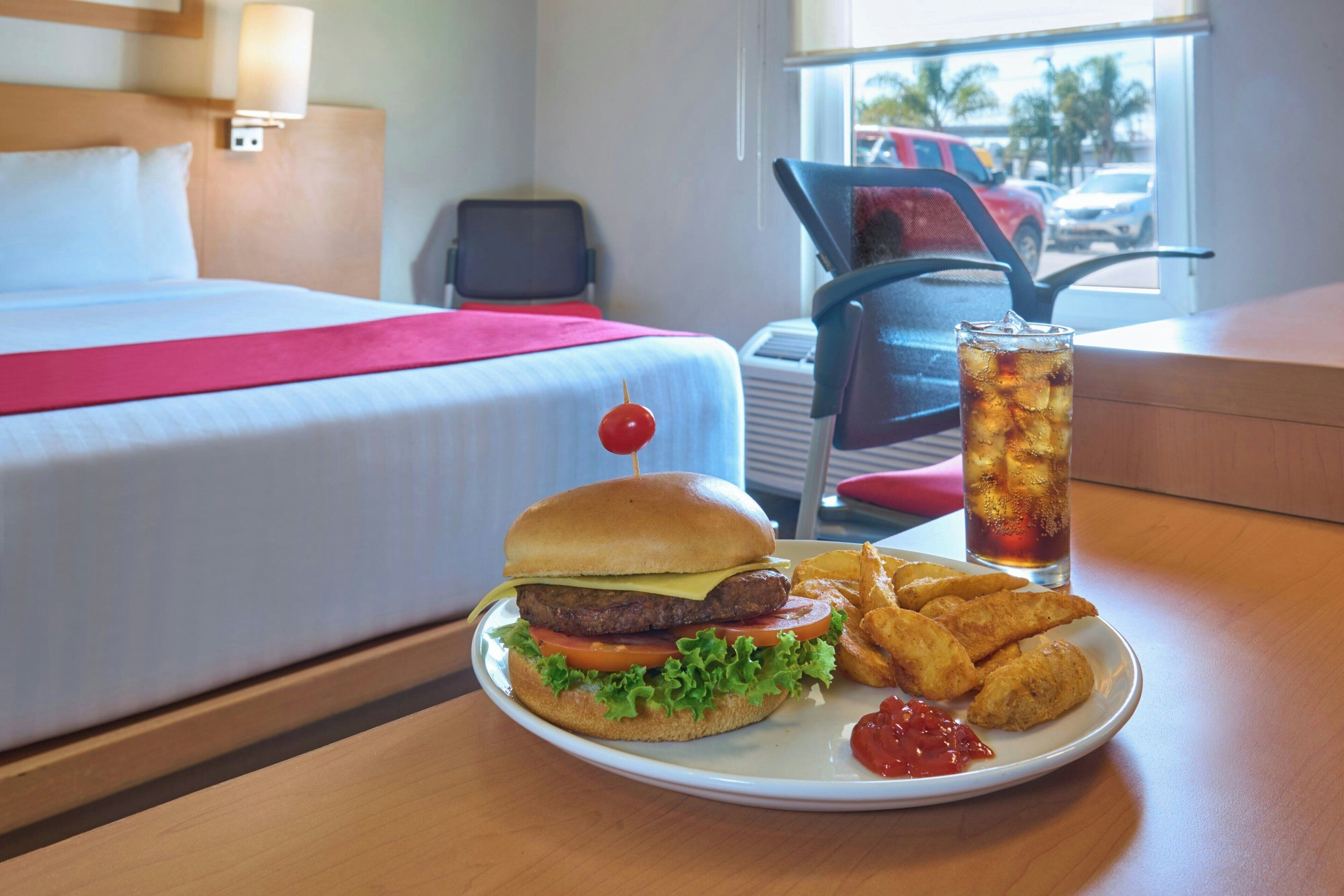 Une chambre d’hôtel avec un lit, une table à manger où est servi un repas, et une vue sur la rue par la fenêtre.