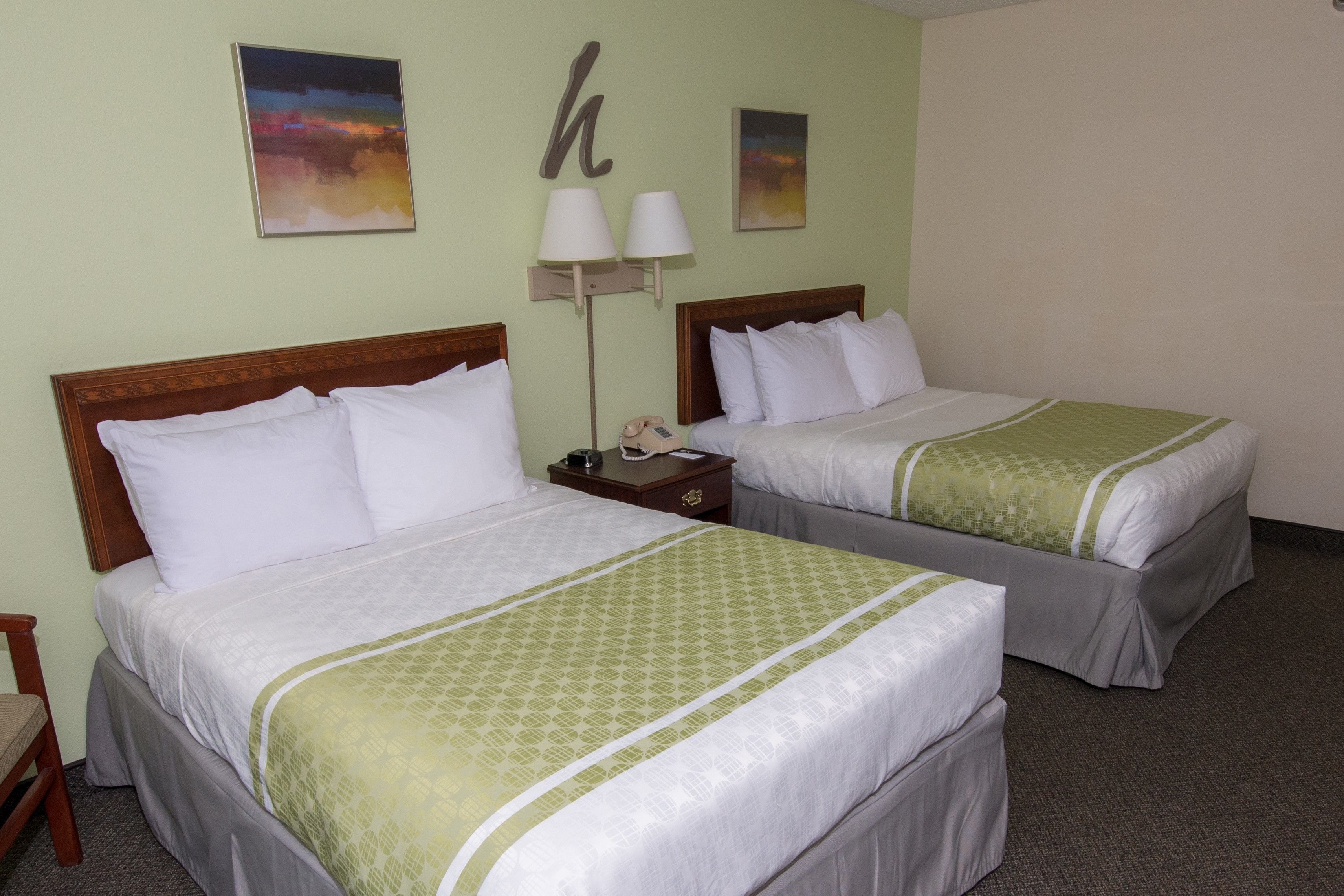 A hotel room with two single beds, a nightstand with a lamp, and a painting on the wall.