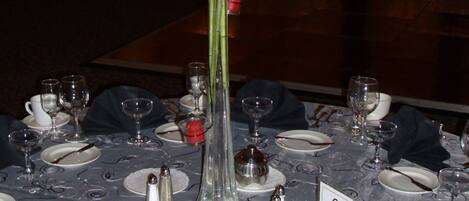 Une table dressée pour un dîner formel, avec de l’argenterie, de la vaisselle blanche et de la verrerie transparente. Un grand vase rempli de fleurs blanches est placé au centre de la table.