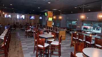 A restaurant with multiple tables and chairs, televisions mounted on the wall, and a wooden floor.