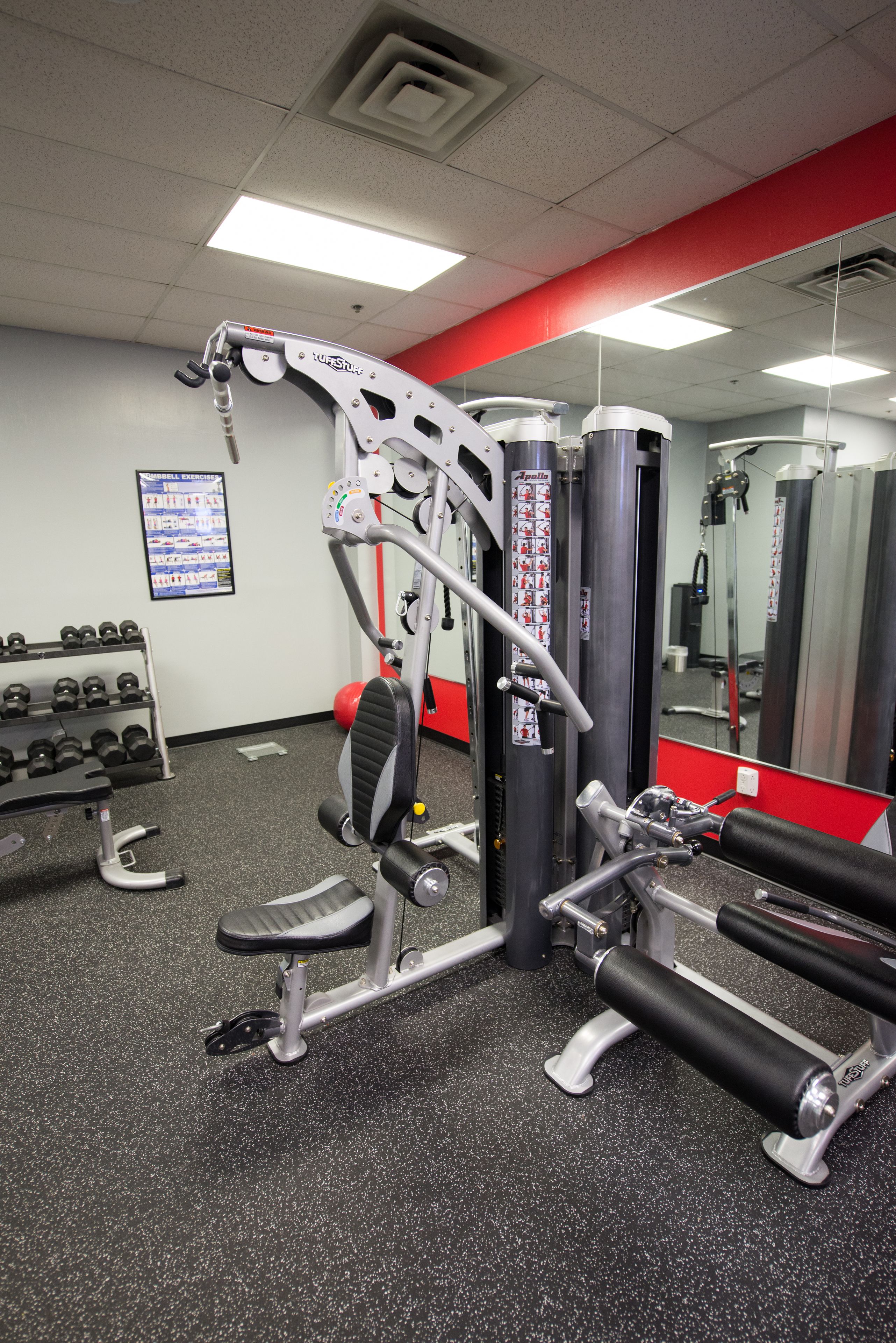 A gym with exercise equipment, a wall-mounted mirror, and a poster on the wall.