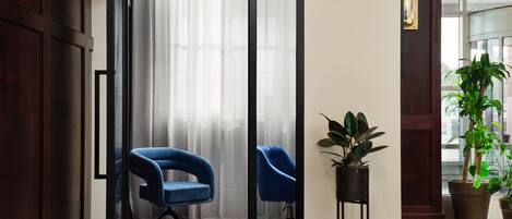 A room with a sliding glass door, two blue chairs, a potted plant, and a wooden floor.