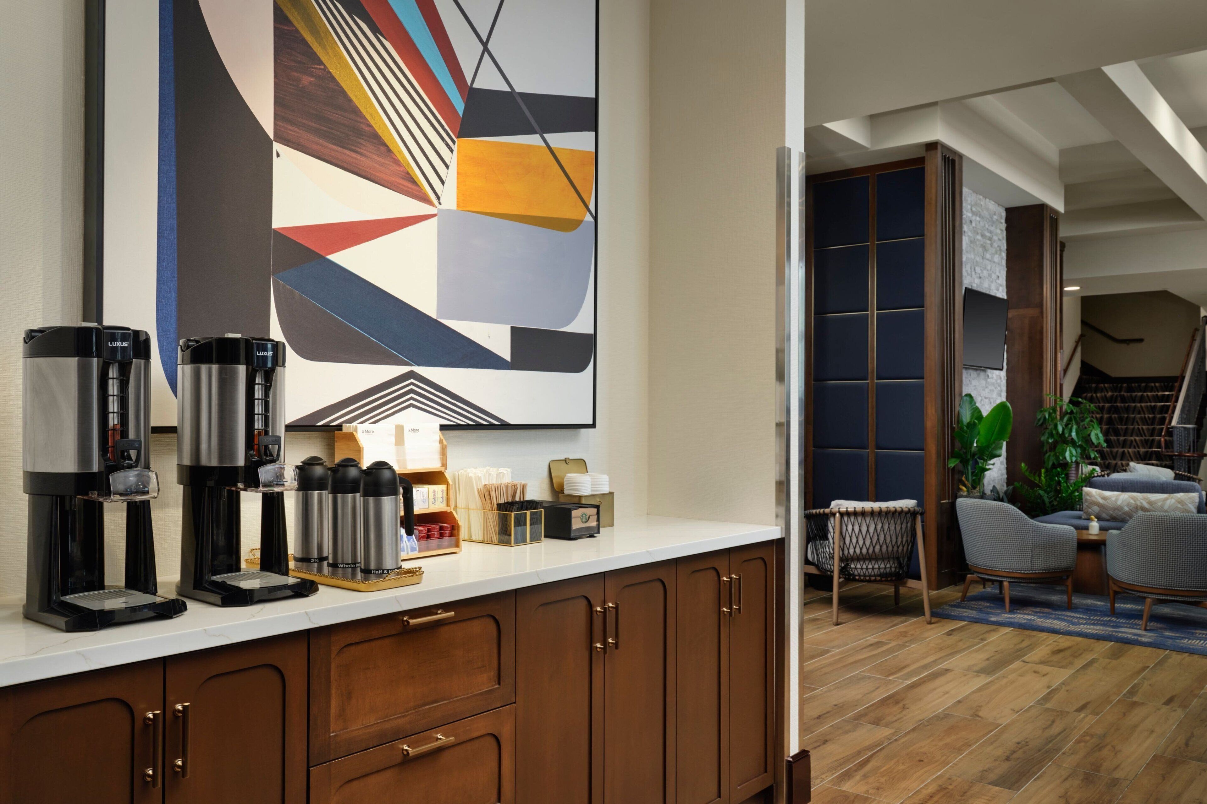 A modern kitchen with two coffee makers, a coffee station, and a large abstract painting on the wall.