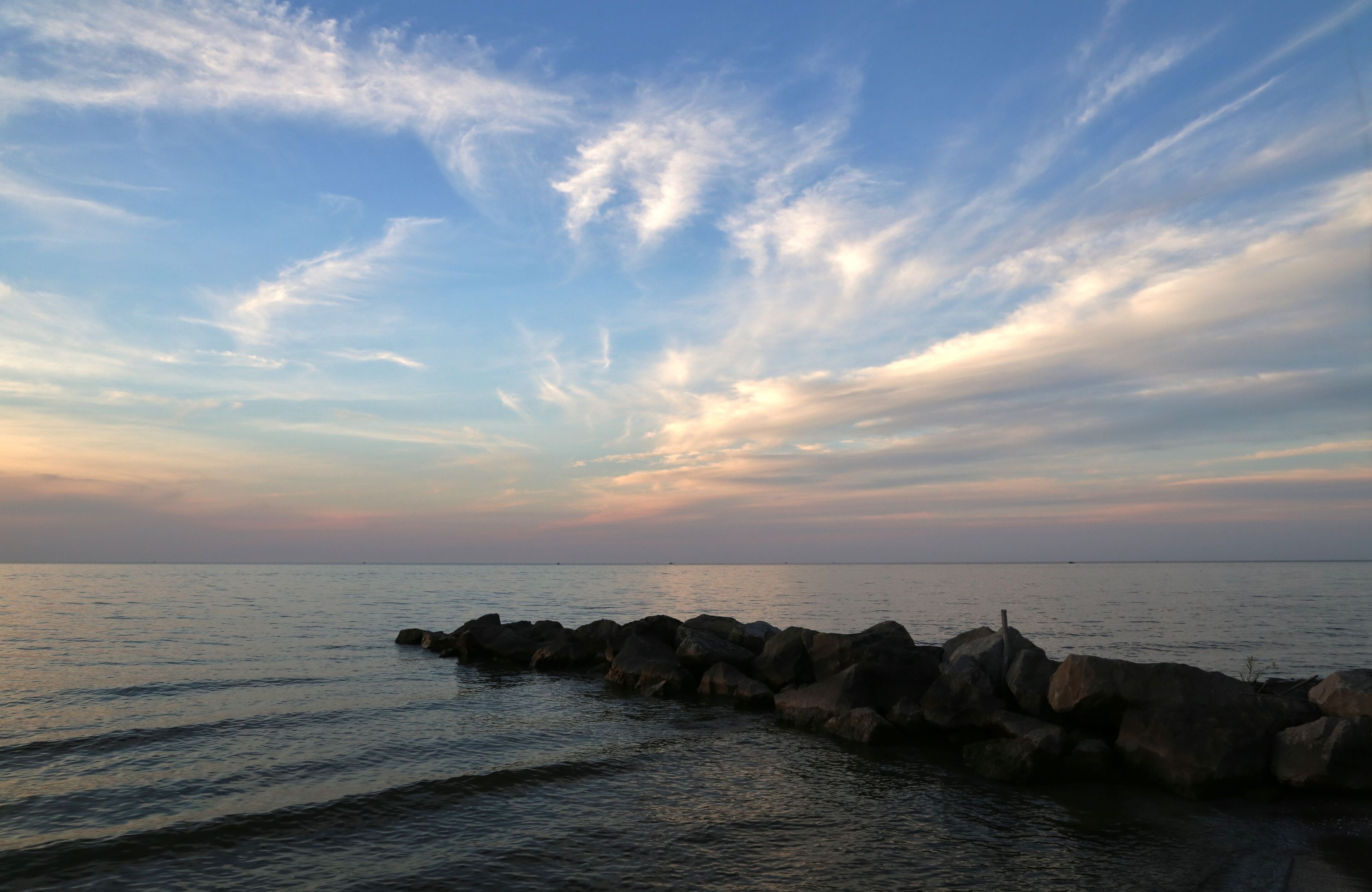A coastal scene with a rocky breakwater and calm sea under a partly cloudy sky.