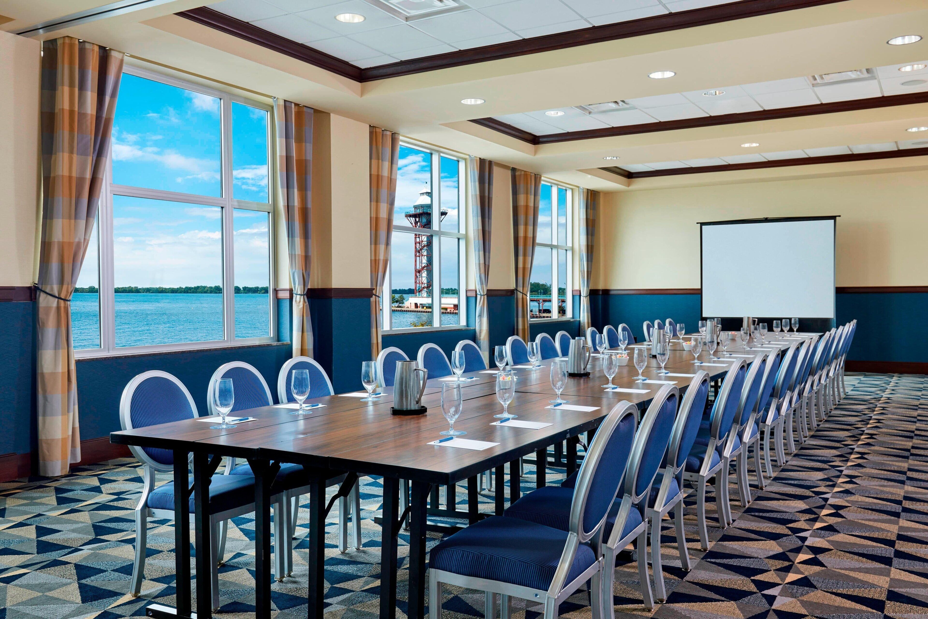 A conference room with a long table, blue chairs, and a projector screen.