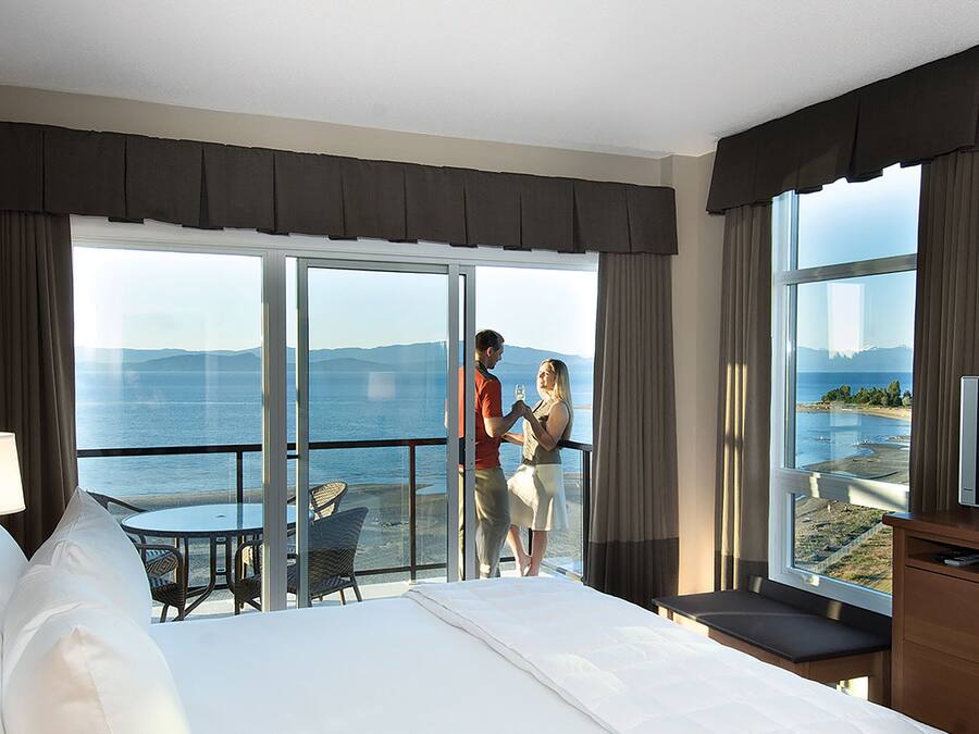 Une chambre d’hôtel dotée d’un grand lit, d’une télévision, d’un balcon avec vue sur la mer et d’un coin repas avec une table et des chaises.