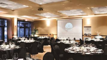 A banquet hall with round tables set for a formal event, a large screen displaying the resort's logo, and a view of the outdoors through large windows.
