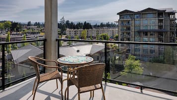 A balcony with wicker chairs and a table, overlooking a residential area with apartment buildings.