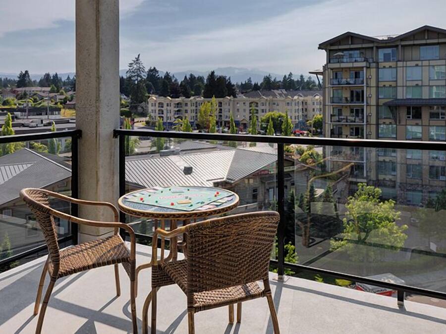 A balcony with wicker chairs and a table, overlooking a residential area with apartment buildings.
