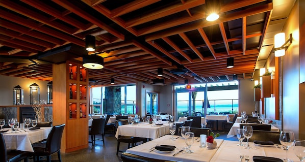 A restaurant with multiple tables, wooden ceiling beams, and large windows offering a view.