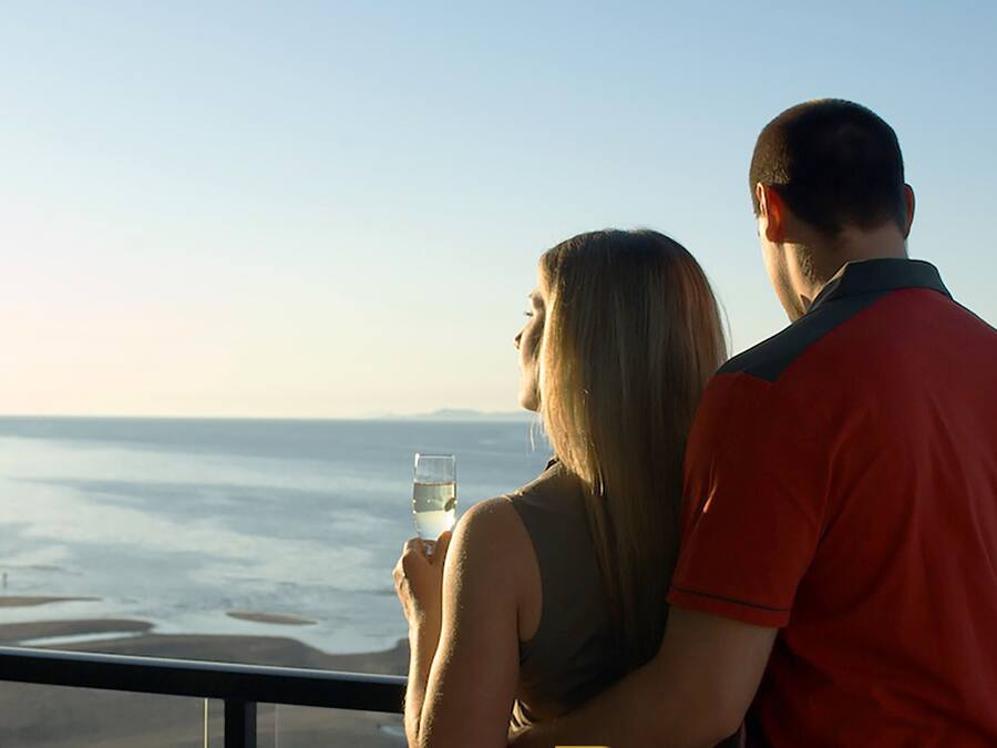 Un couple admire un paysage côtier depuis un balcon.