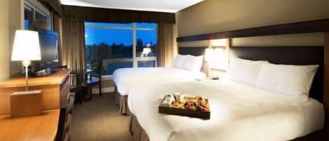 A hotel room with two beds, a desk, and a window with a view of the outdoors.