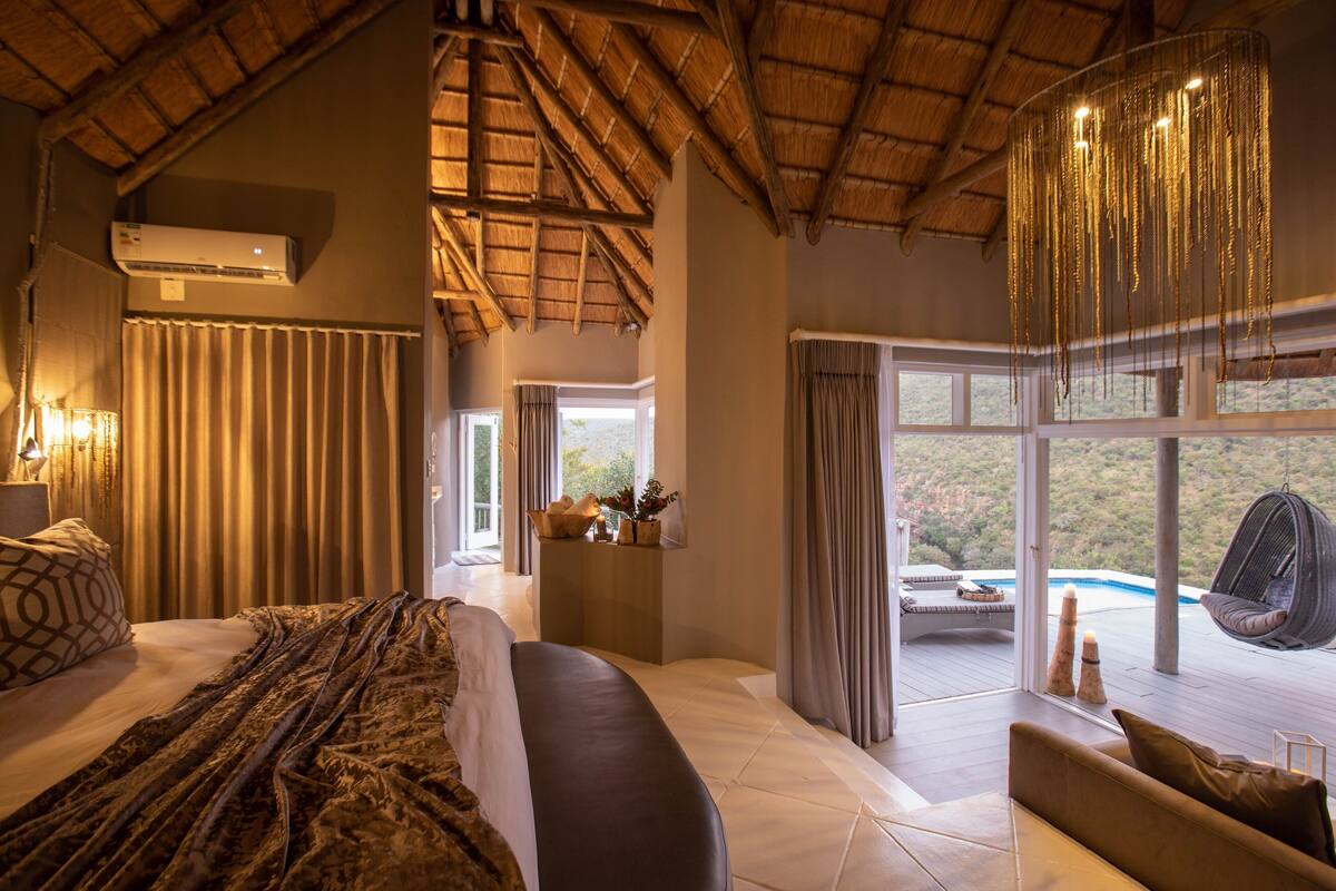 Ein geräumiges Schlafzimmer mit einem großen Bett, einem Hängesessel und Blick auf einen Pool.