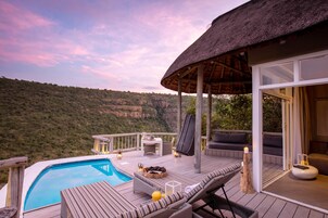 Un área junto a la piscina con techo de paja, sillas de descanso y vistas a un paisaje montañoso.