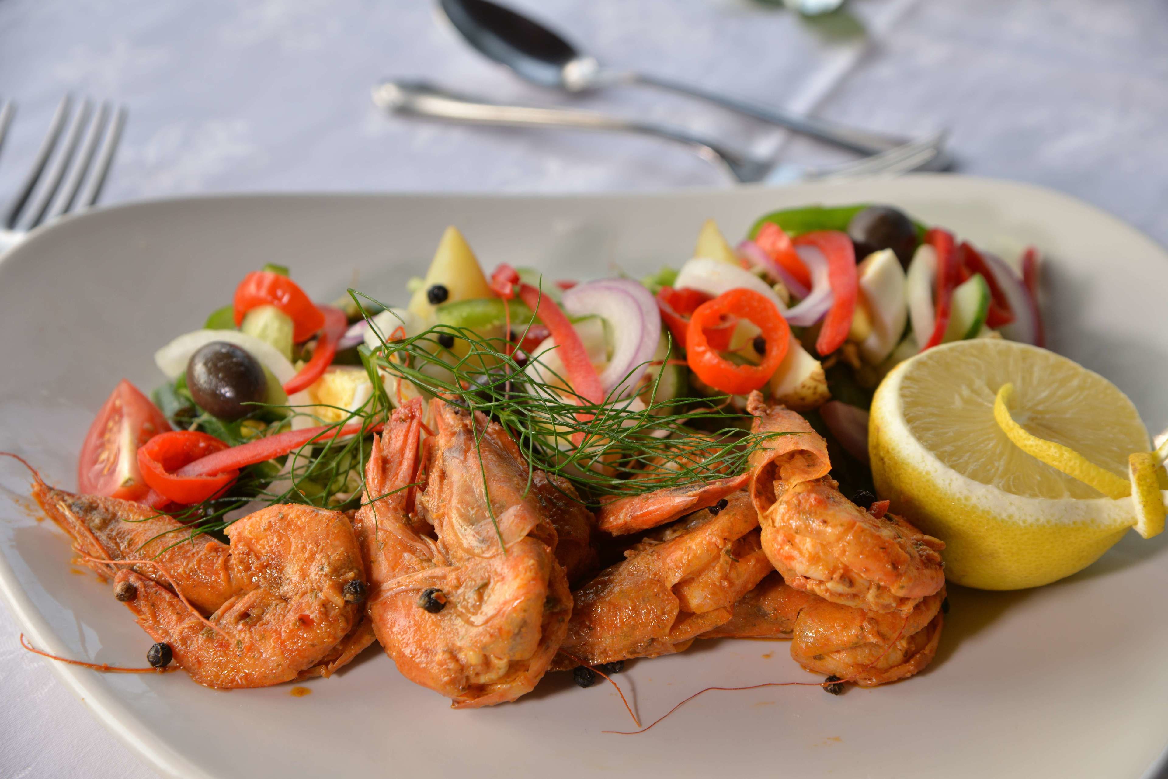 A plate of cooked shrimp with a lemon wedge and a salad of mixed vegetables.