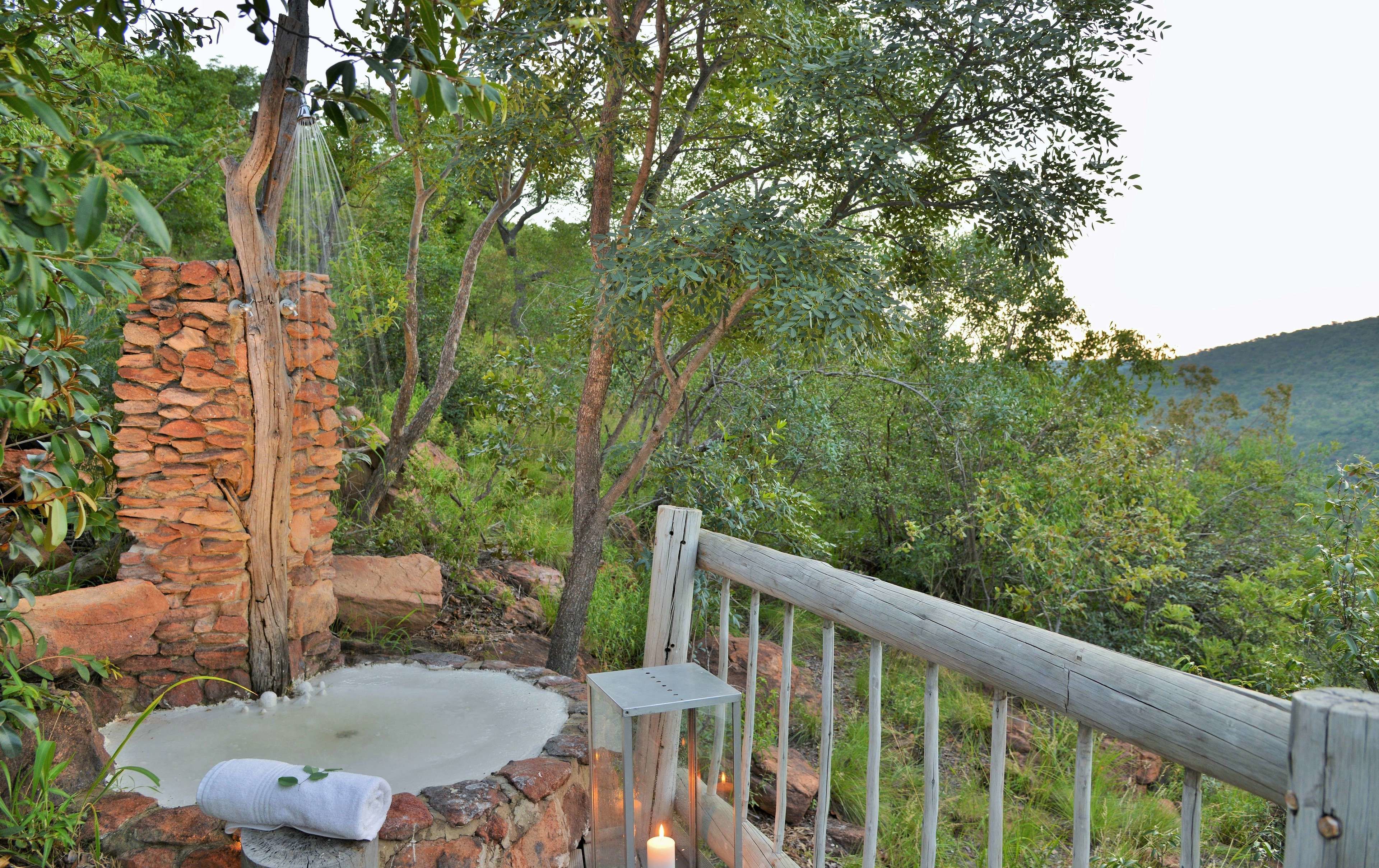 A rustic outdoor setting with a stone wall, a wooden bench, and a wooden railing overlooking a lush green landscape.