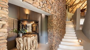 Una escalera de escalones blancos conduce a un segundo piso, flanqueada por muros de piedra y una mesa de madera con una planta.