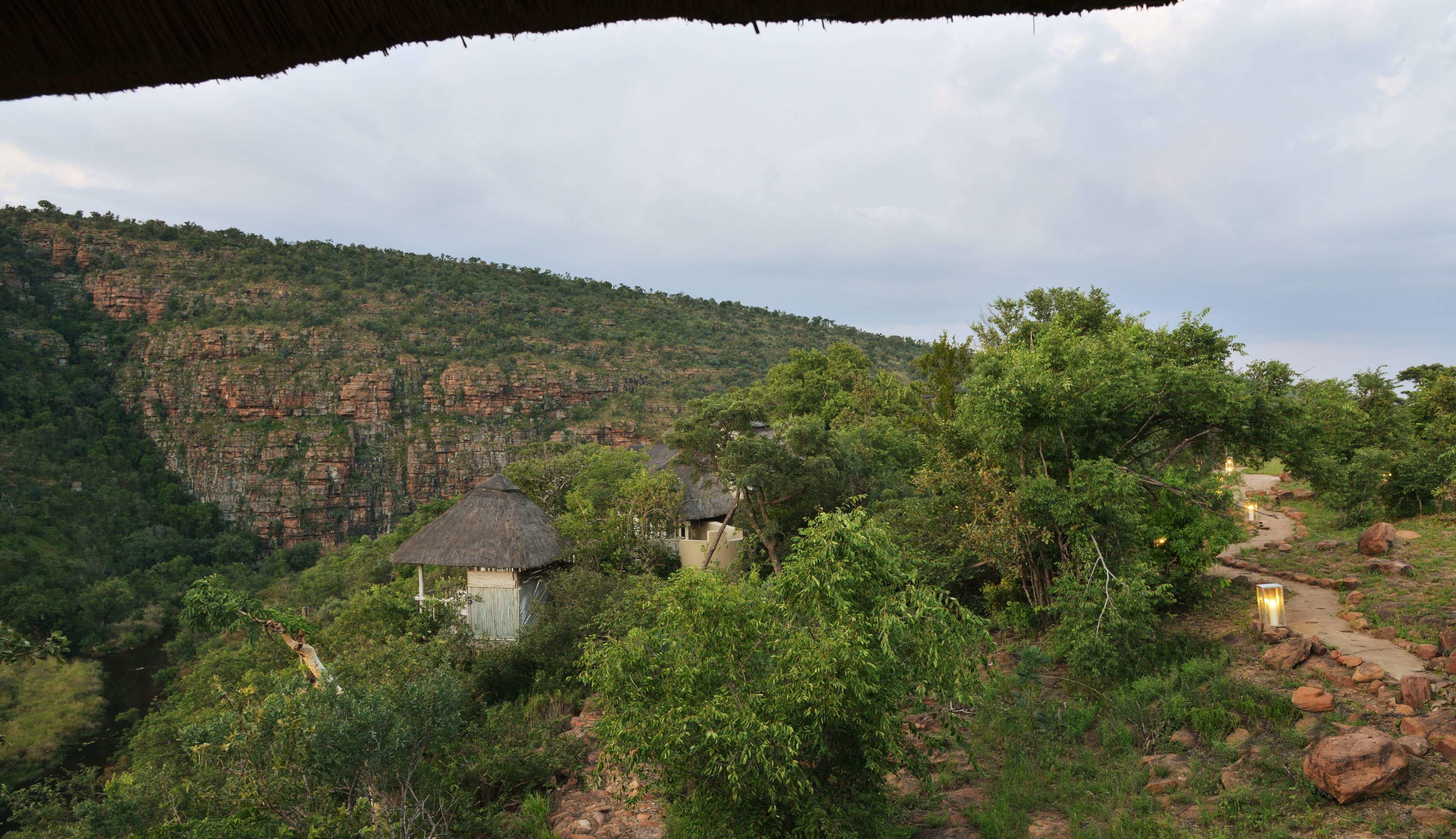 A rustic lodge with thatched-roof cabins nestled among dense greenery and rocky cliffs.