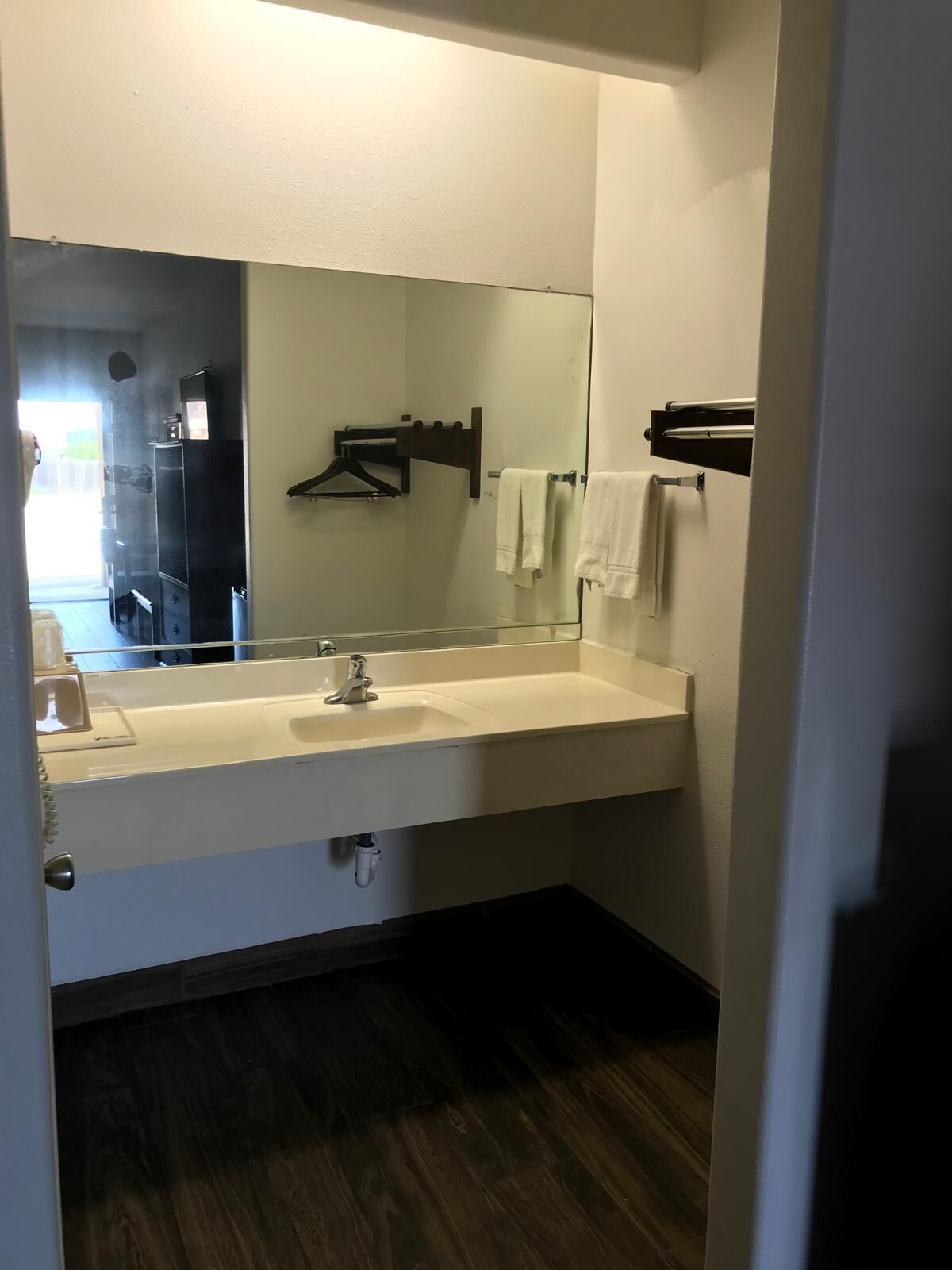 A bathroom with a white sink, a mirror, and a dark wooden floor.