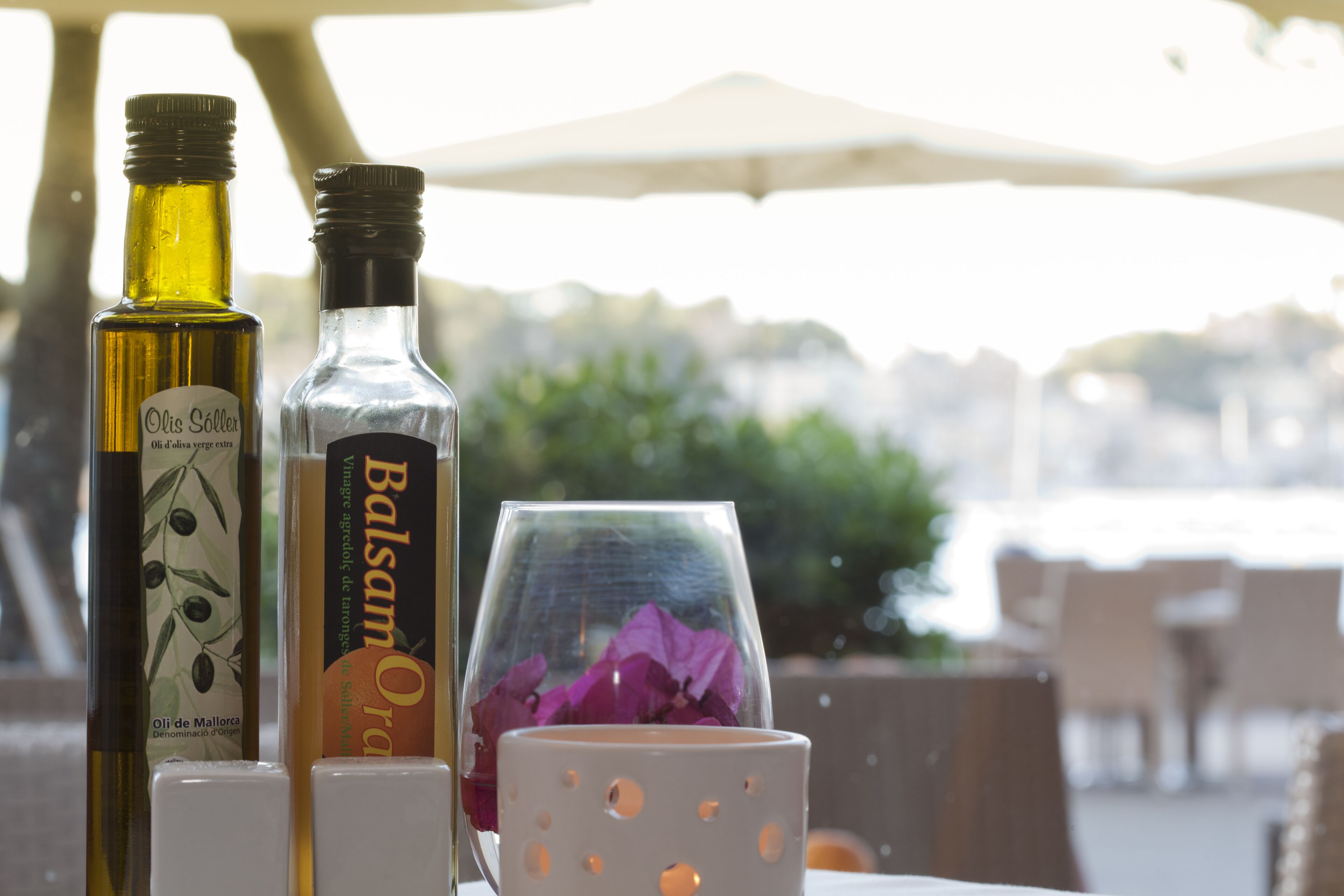 A table with two bottles of olive oil and a glass with purple flowers.